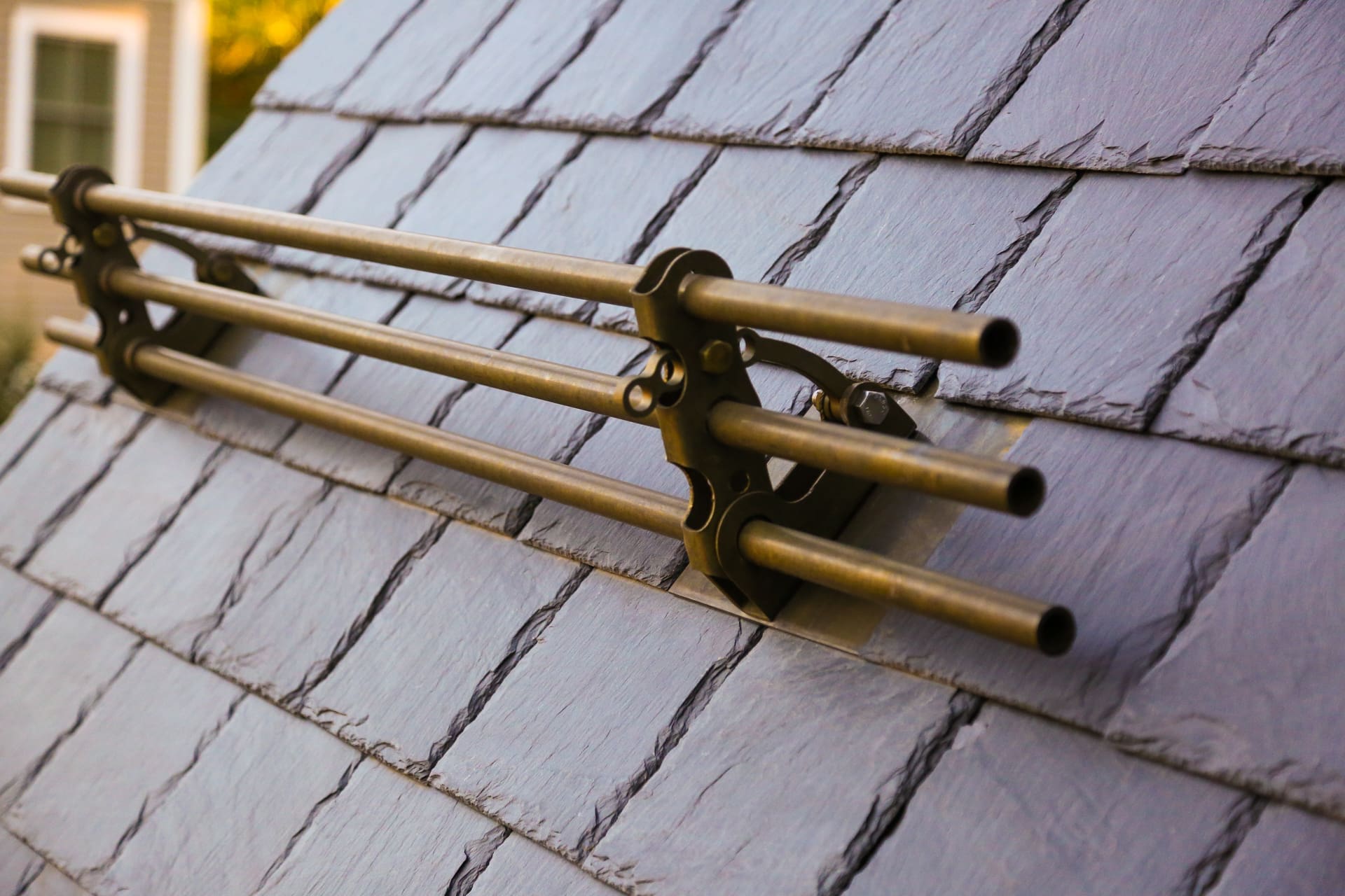 A photo of a brass snow rail bracket on a black stone slate tile roof.