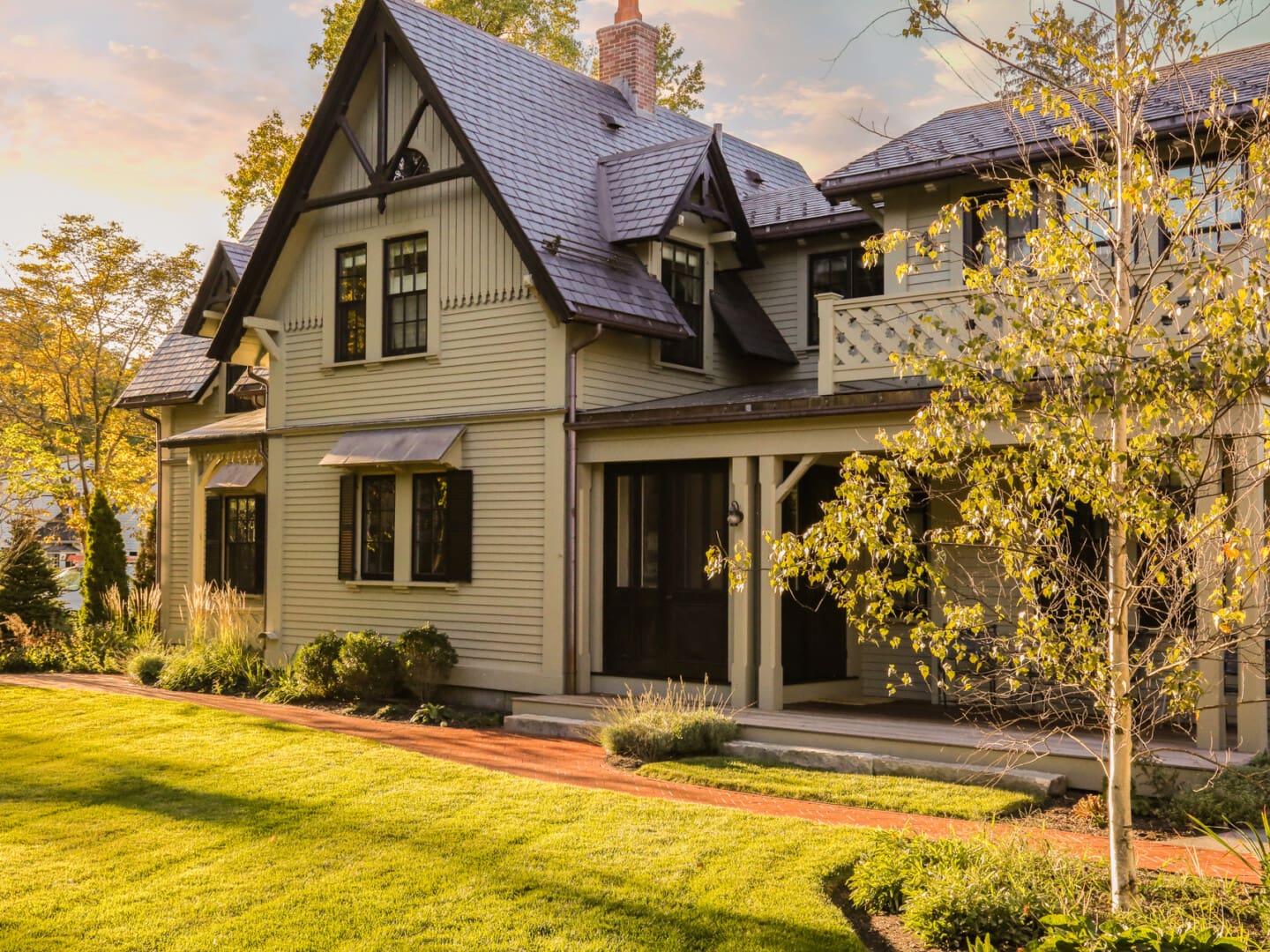 A photo of a house with grey-green painted siding, stone shingle roofing, antique black gable brackets, and painted colonial detailing.