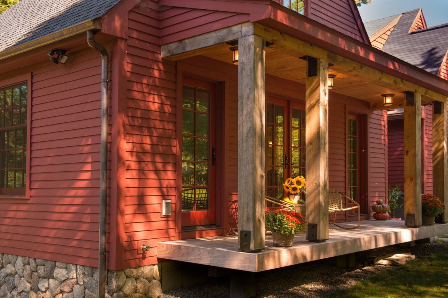 A photo of a house with dark red siding, and a front porch made of natural wood with black metal hardware.