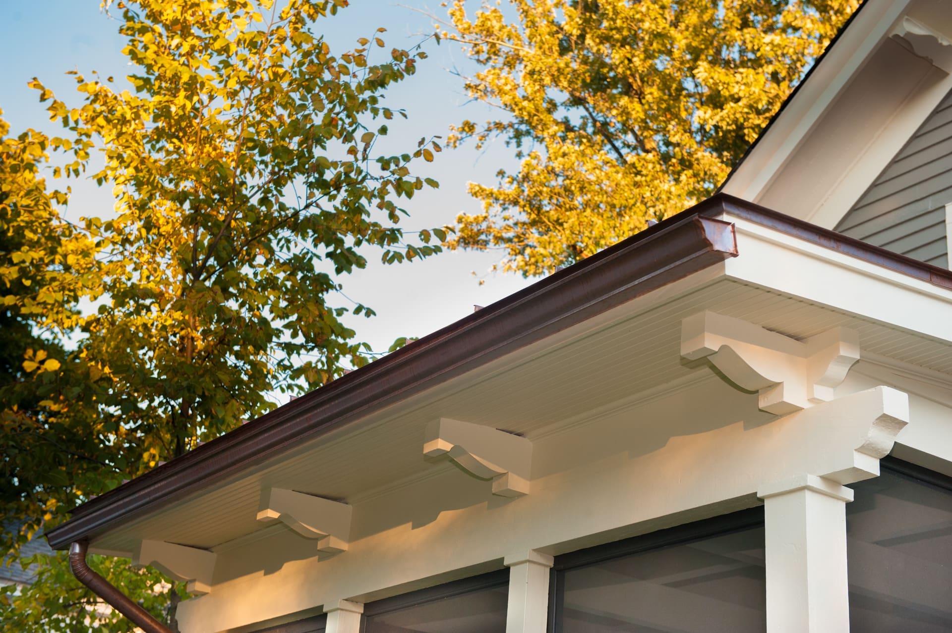 A photo of a white-painted closed roof overhang with carved white-painted support brackets over a screened-in porch.