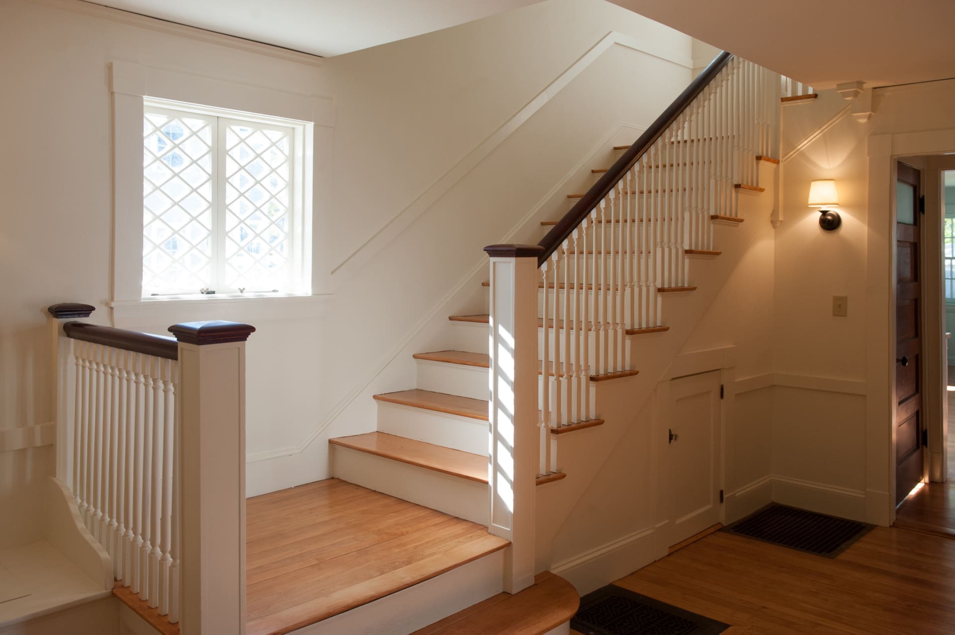 A photo of a staircase with hardwood steps, a dark wooden railing and white rail posts.