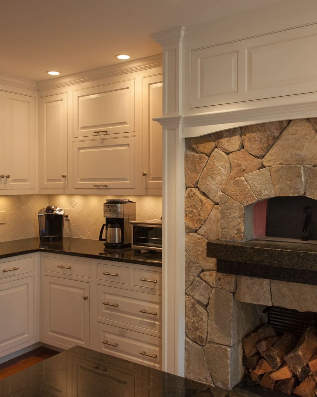 A photo of a kitchen with white raised panel cabinets, black marble countertops, and a built-in, stone wood-fired oven.