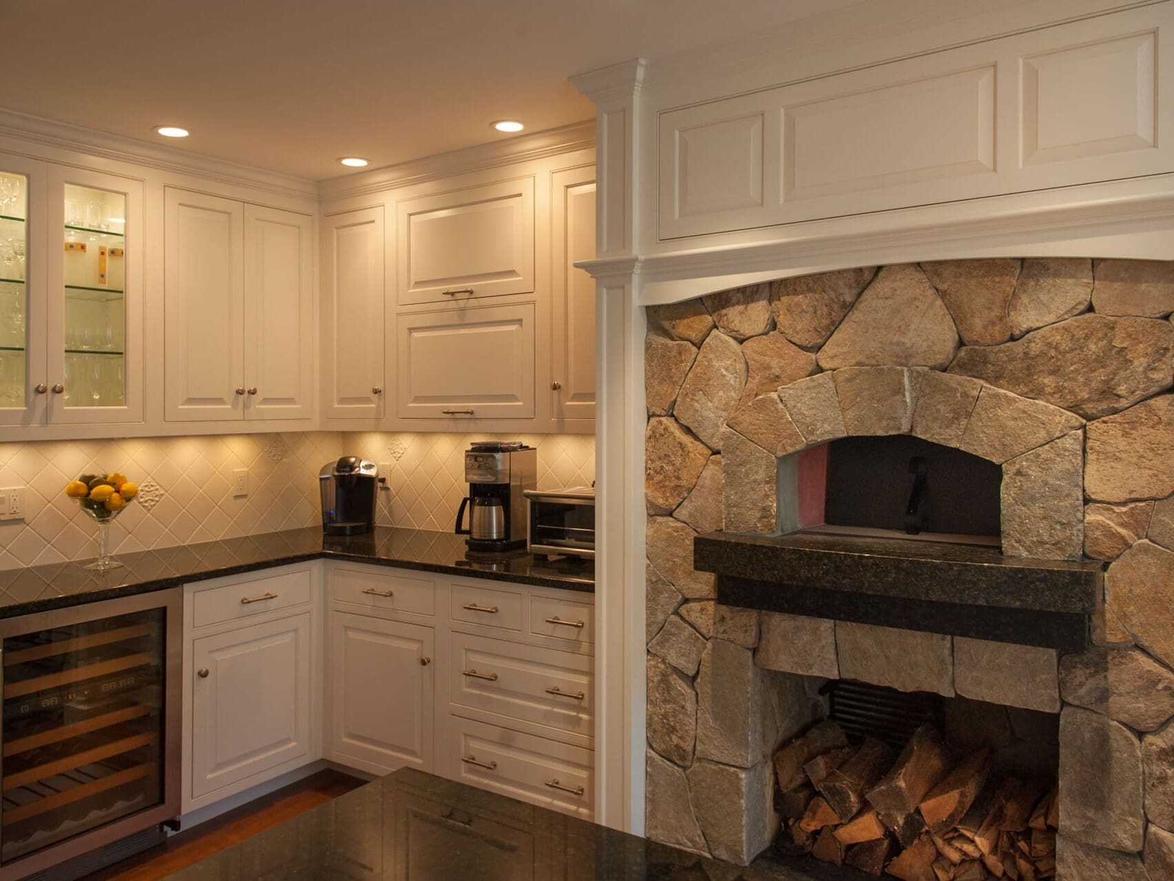 A photo of a kitchen with white raised panel cabinets, black marble countertops, and a built-in, stone wood-fired oven.