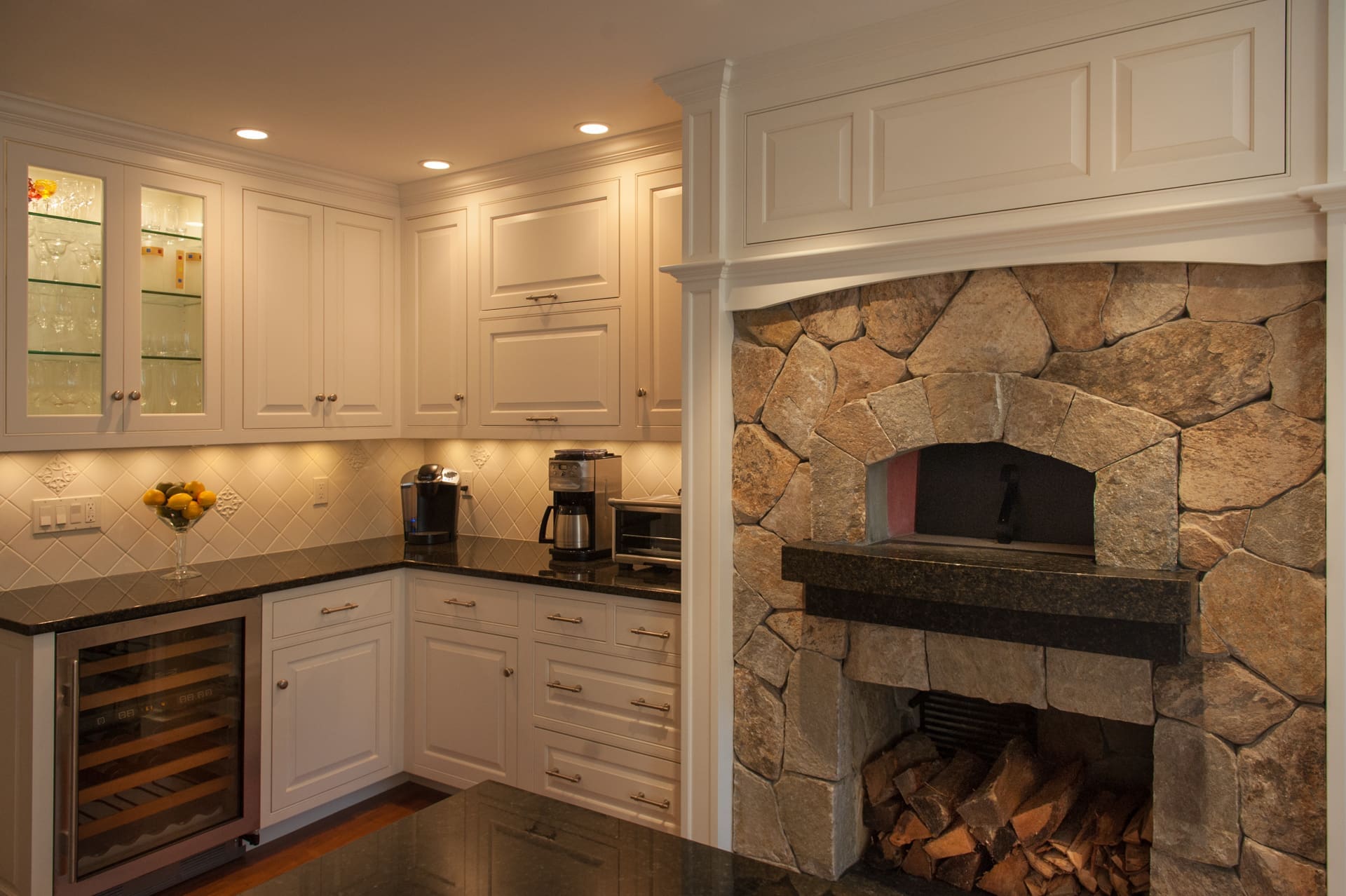 A photo of a kitchen with white raised panel cabinets, black marble countertops, and a built-in, stone wood-fired oven.