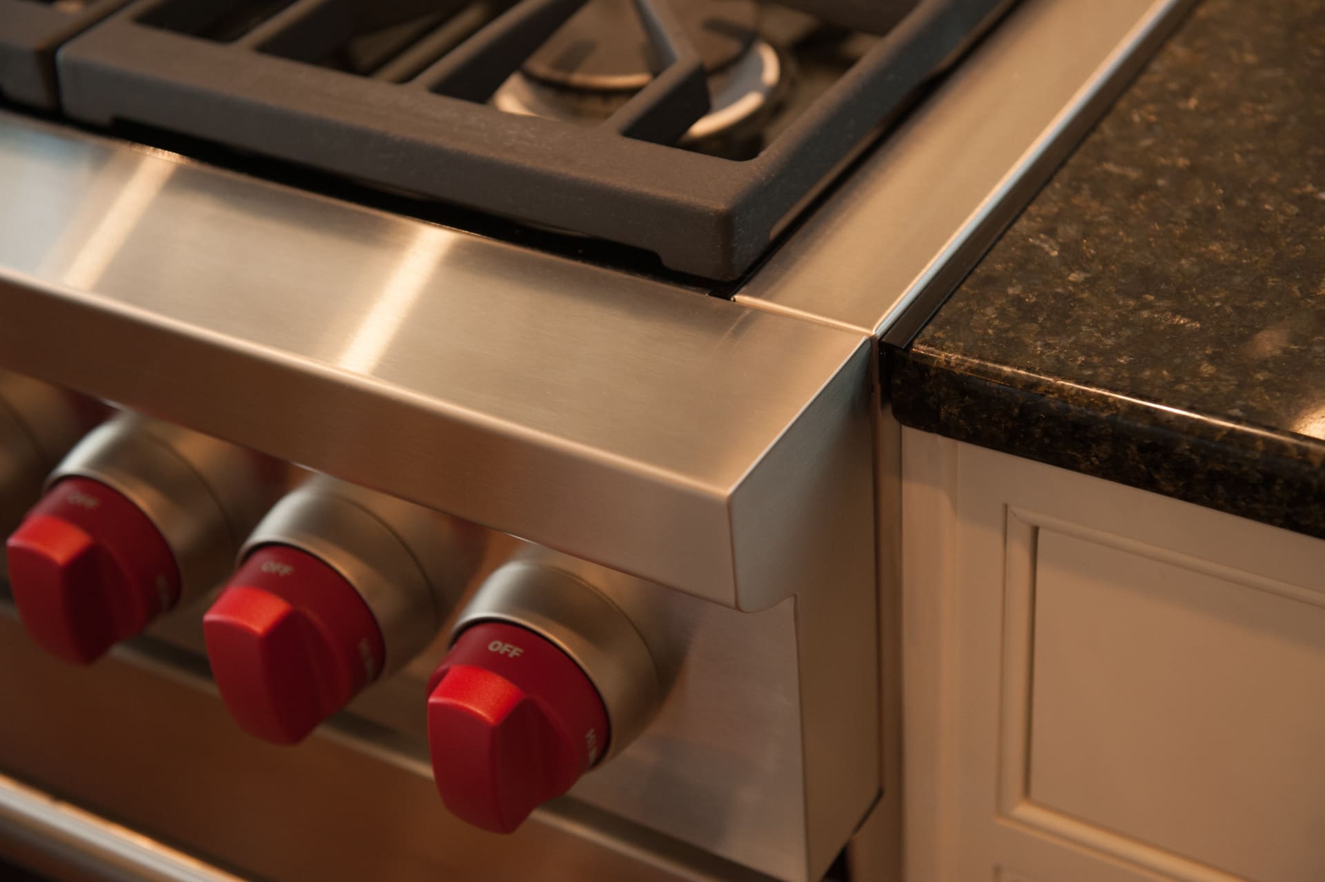 A closeup photo of a stainless steel oven and stovetop attached to a black stone countertop and white shaker-style cabinets.