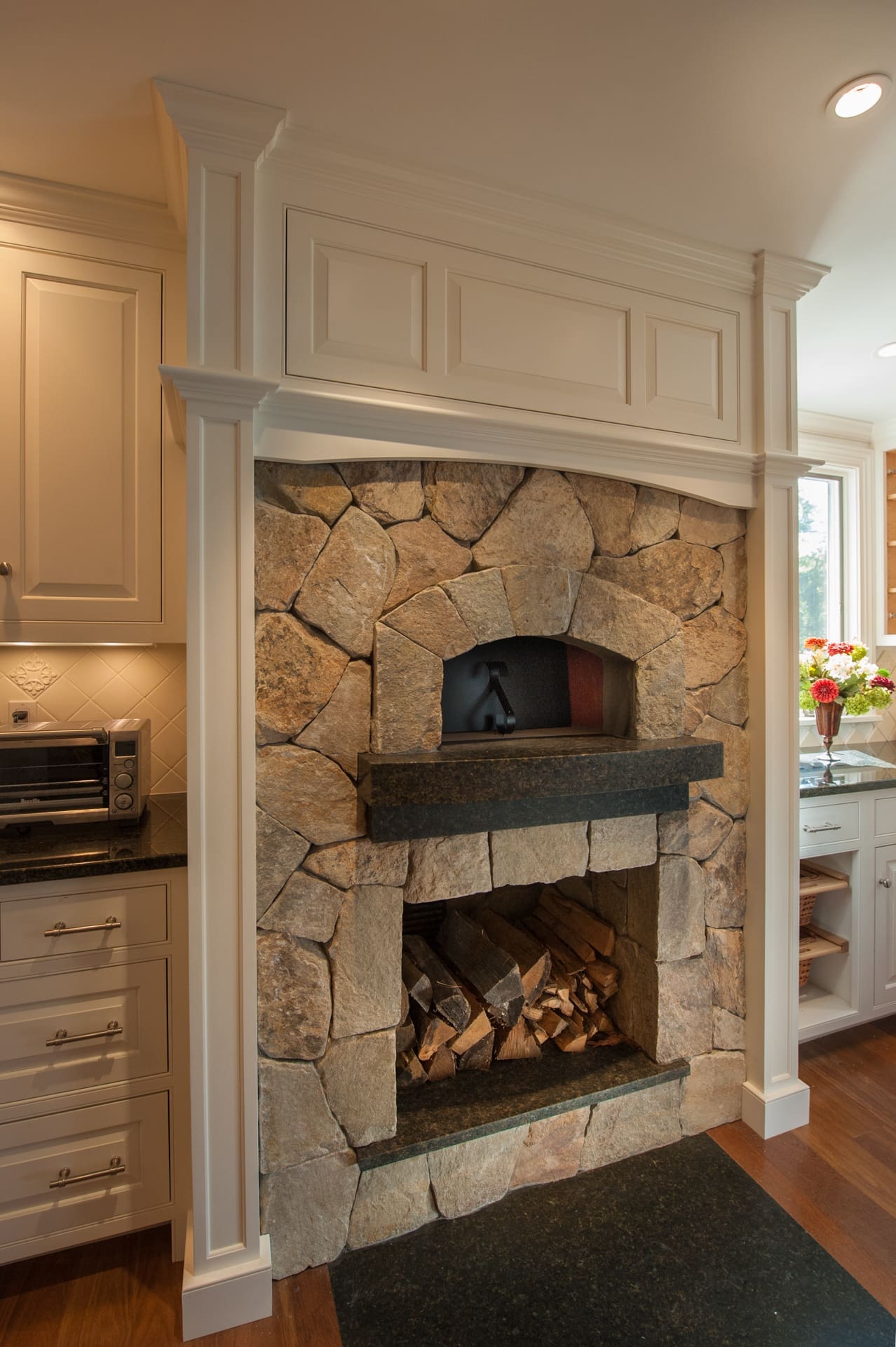 A photo of a built-in, stone wood-fired oven with wood storage and black marble counters.