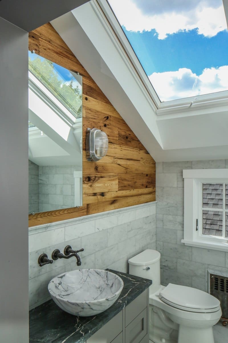 A photo of a bathroom with marble tile, rubbed brass hardware, reclaimed wood walls, and a skylight.