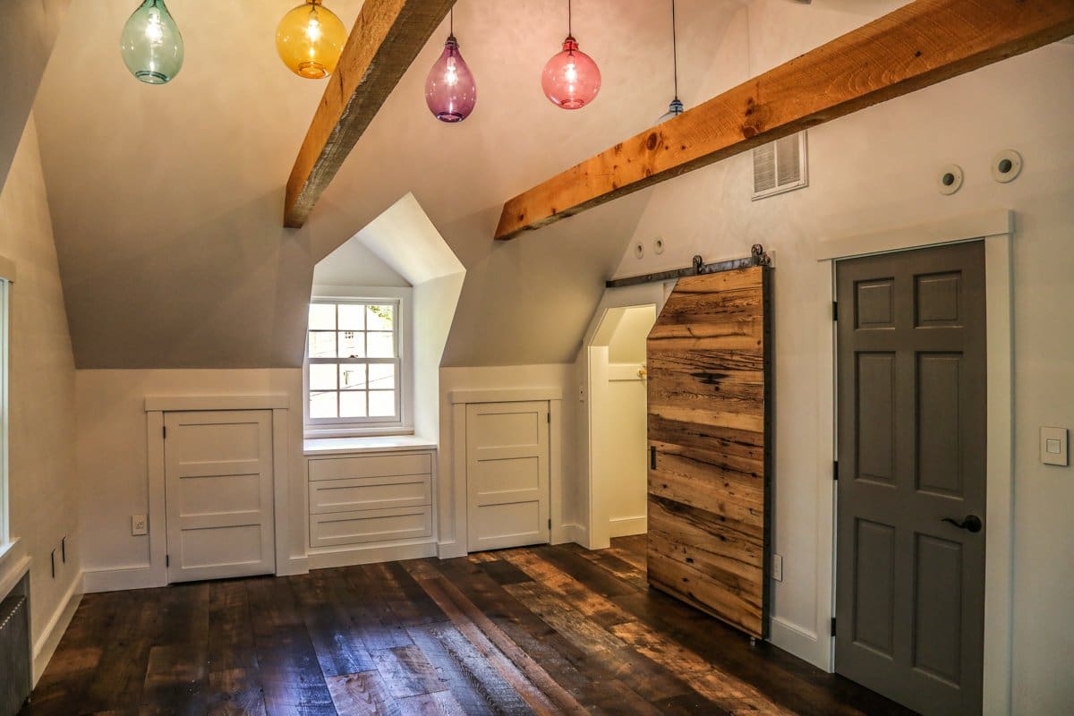 A photo of a room with vaulted ceilings, reclaimed hardwood floors, a sliding barn door, wooden beams, and a multicolored series of hanging light fixtures.