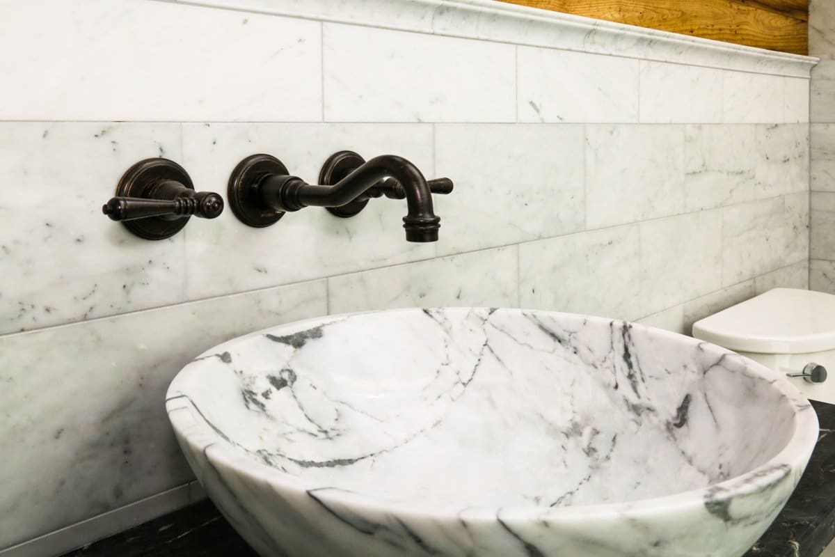 A photo of a bathroom sink with a large marble bowl, rubbed bronze hardware, and marble tile.