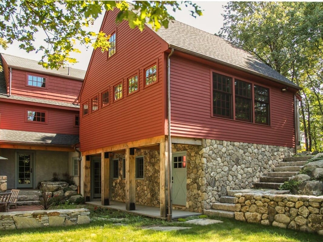 A photo of a red barn-style addition with a stone first level and an overhang supported by wooden beams.
