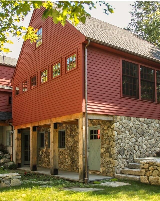 A photo of a red barn-style addition with a stone first level and an overhang supported by wooden beams.