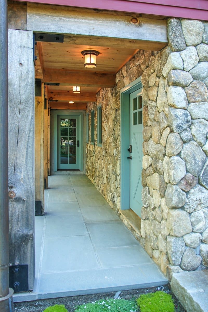A photo of a walkway with slate floors and wooden beams connecting two below-ground teal exit doors.