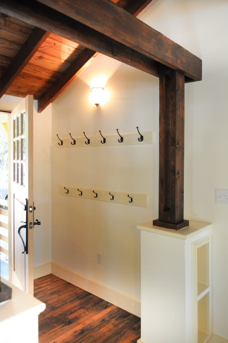 A photo of an entryway with built-in storage, clothing hangers, vaulted wooden ceilings, wooden floors, and wooden beams.