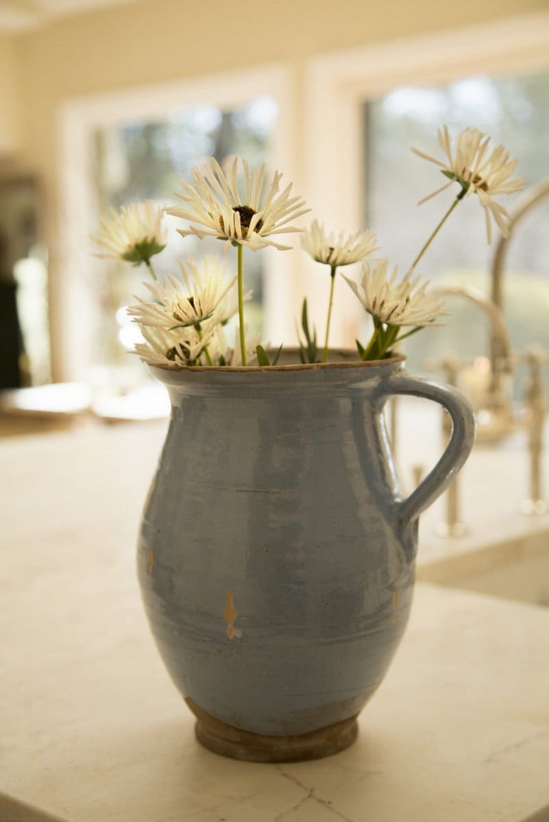 A photo of a periwinkle vase with daisies on a marble kitchen island.