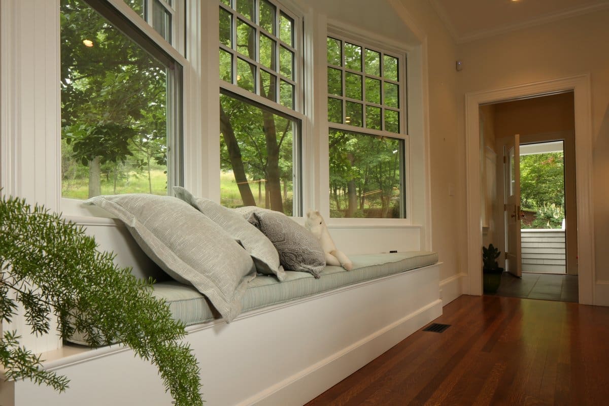 A photo of a window nook with sea foam colored cushions and pillows.