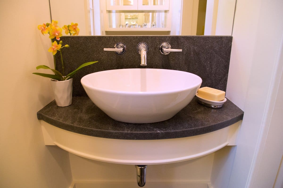 A photo of a floating bathroom sink vanity with a large porcelain bowl, metal faucet, and black stone counter.