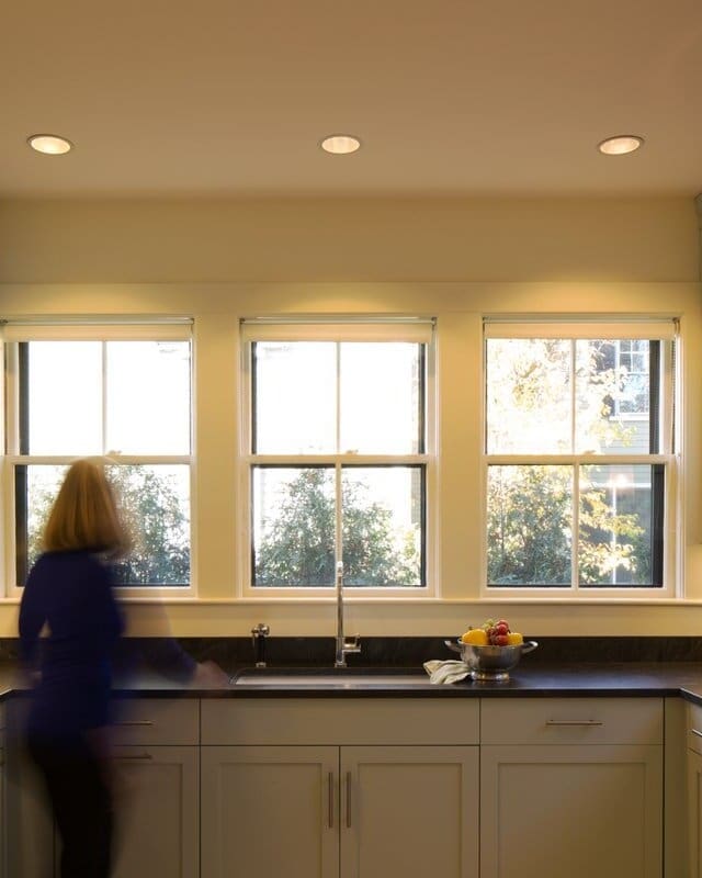 A photo of a kitchen with black stone countertops and faded green painted shaker-style cabinets.