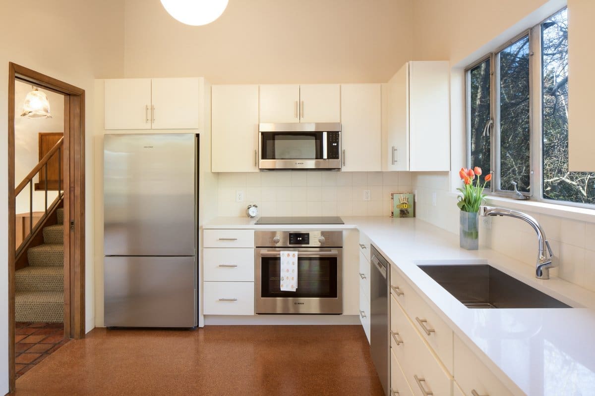 A photo of a kitchen with white cabinets, white square tile, and stainless steel appliances.