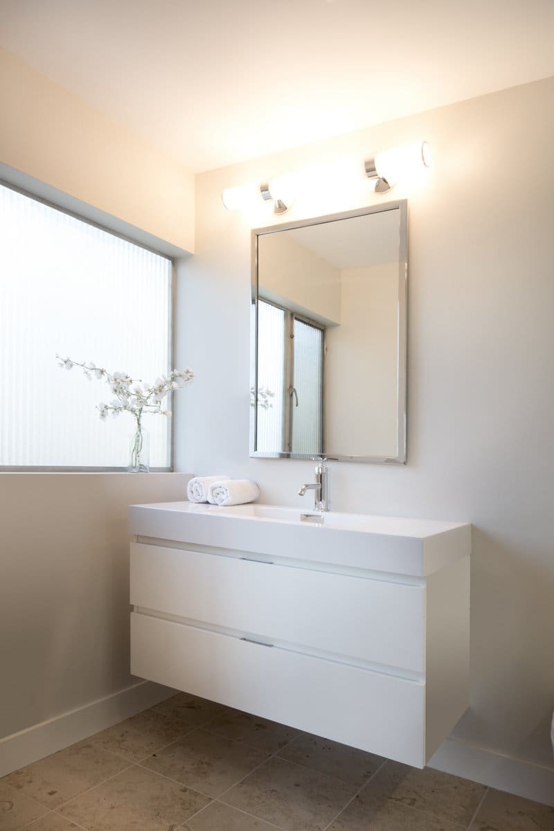 A photo of a bathroom with white walls and a floating white vanity with large porcelain sink and hanging mirror.