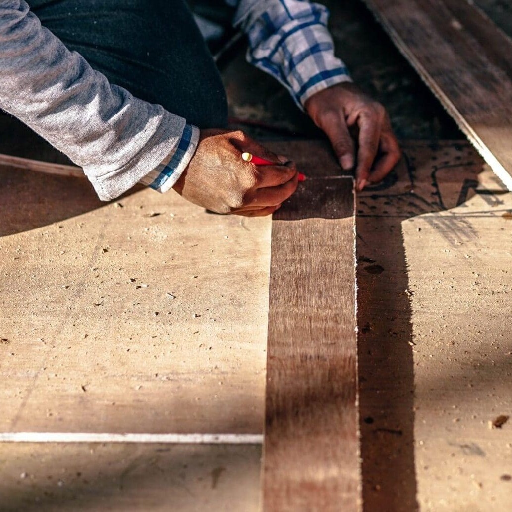 A photo of a construction worker marking a piece of wood with a pencil.