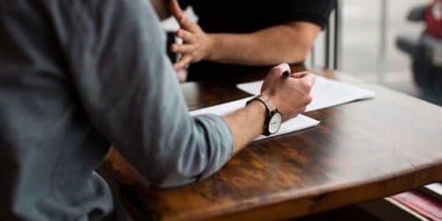 Photo of two people talking, one is listening and taking notes.