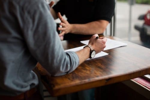 Photo of two people talking, one is listening and taking notes.