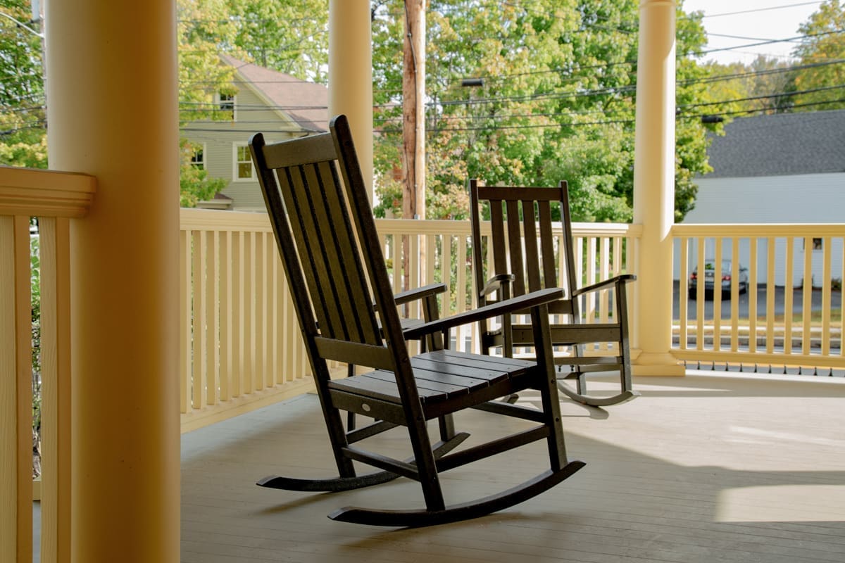 A photo of two black rocking chairs on a front deck with yellow columns and railings.
