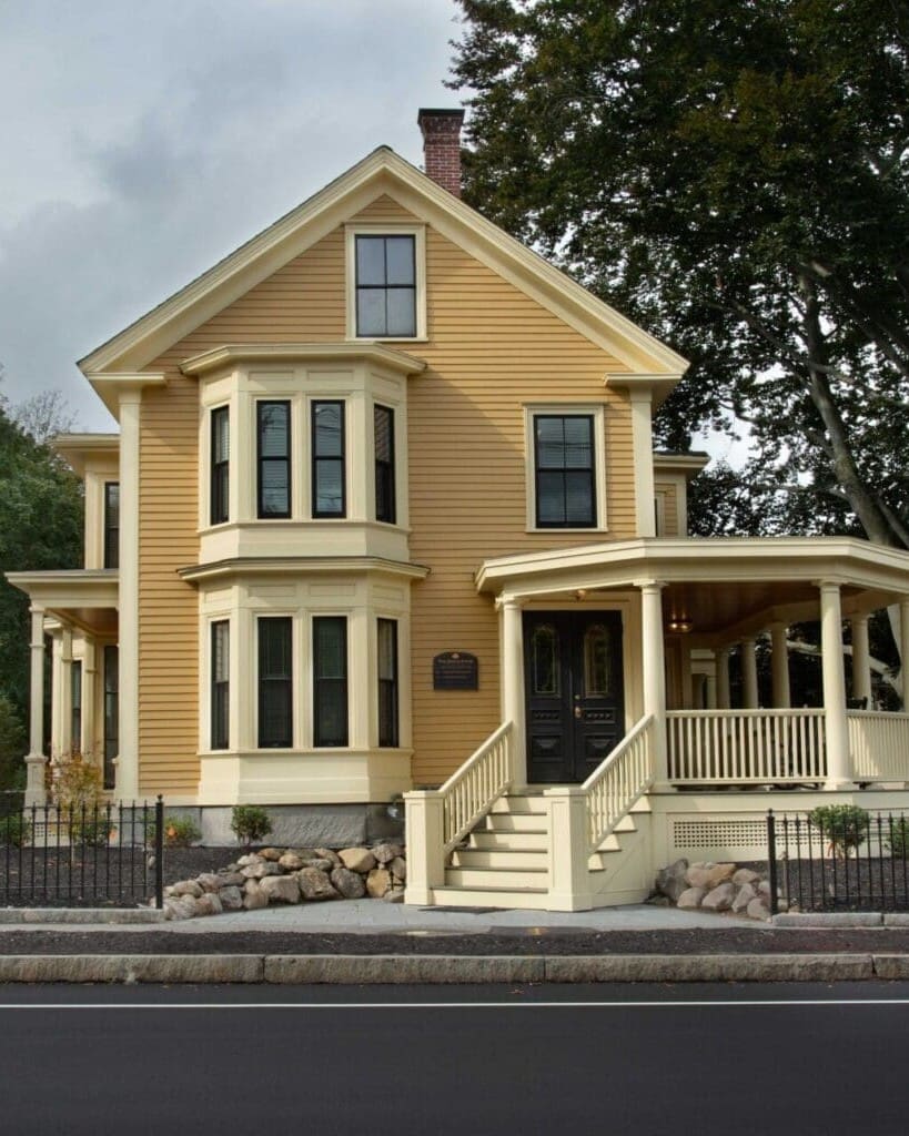 A photo of a yellow building with a front porch with yellow columns and railings from street view.