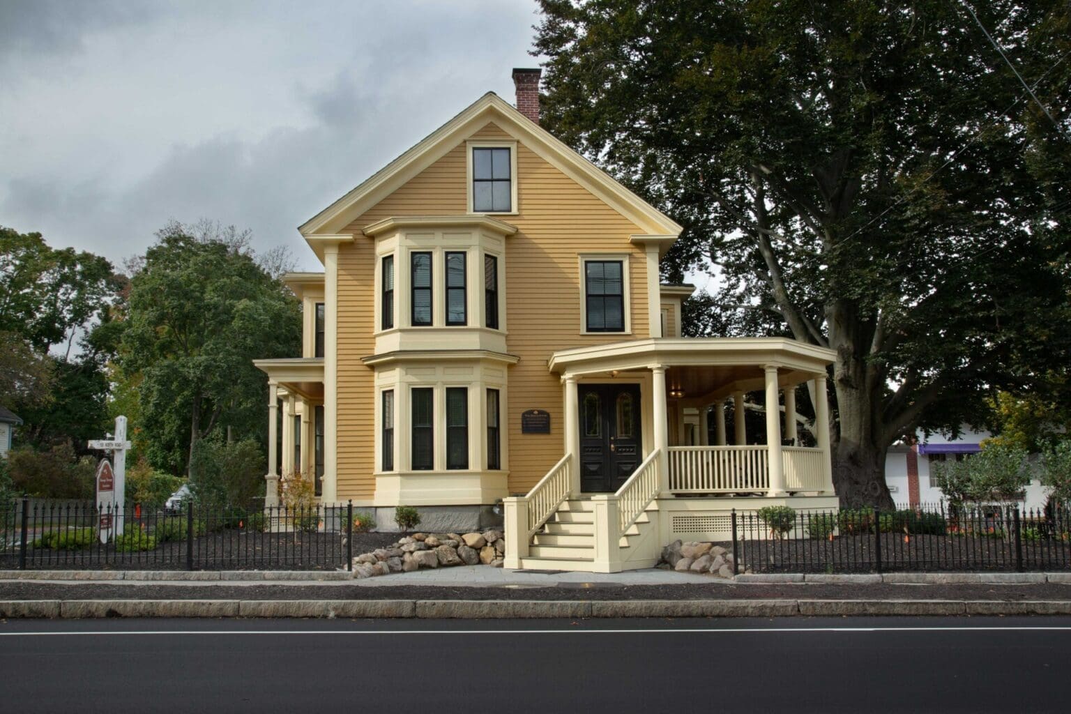 A photo of a yellow building with a front porch with yellow columns and railings from street view.