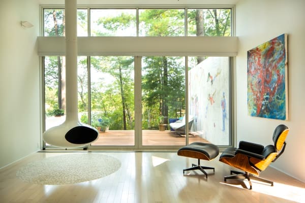 a photo of a mid-century modern home with floor-to-ceiling windows, a hanging oval-shaped fireplace, and an Eames chair.