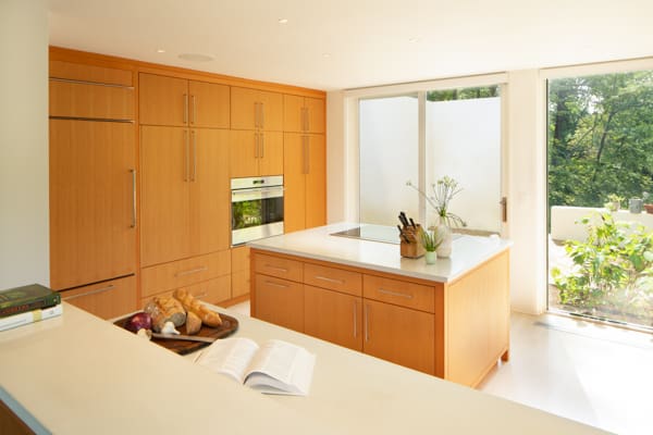 A photo of a midcentury modern kitchen with built-in appliances and wooden cabinets, island, and white marble countertops.