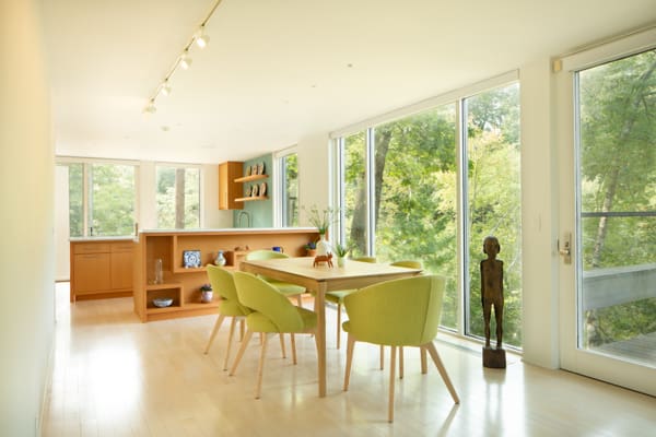 A photo of a mid-century modern dining room with green chairs and large windows.