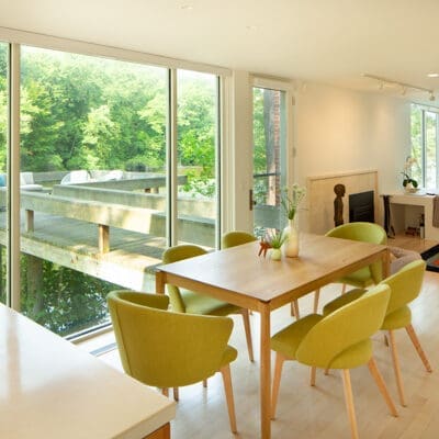 A photo of a dining room table with six light green chairs and windows looking out onto a the water and an outdoor seating area.