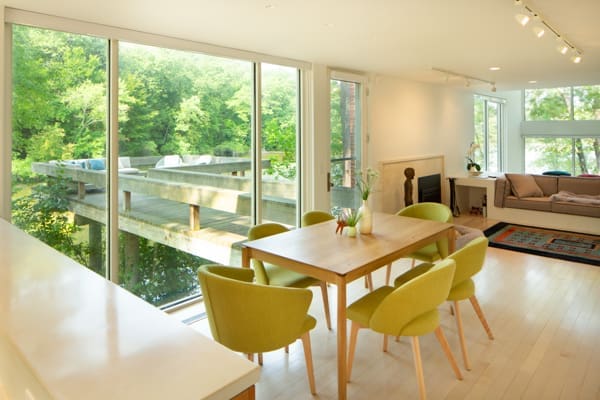 A photo of a dining room table with six light green chairs and windows looking out onto a the water and an outdoor seating area.