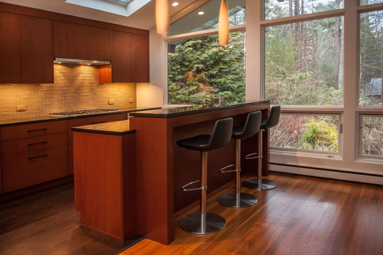 A photo of a mid-century modern kitchen with cherry wood cabinetry and island, black stone countertops, and stainless steel appliances.