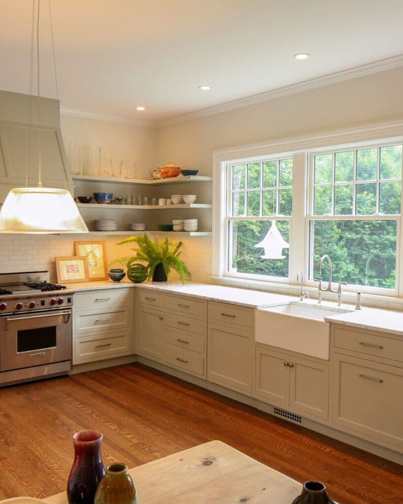 A photo of a classic kitchen with shaker-style cabinets, a large porcelain sink, stainless steel appliances, and a bank of windows.
