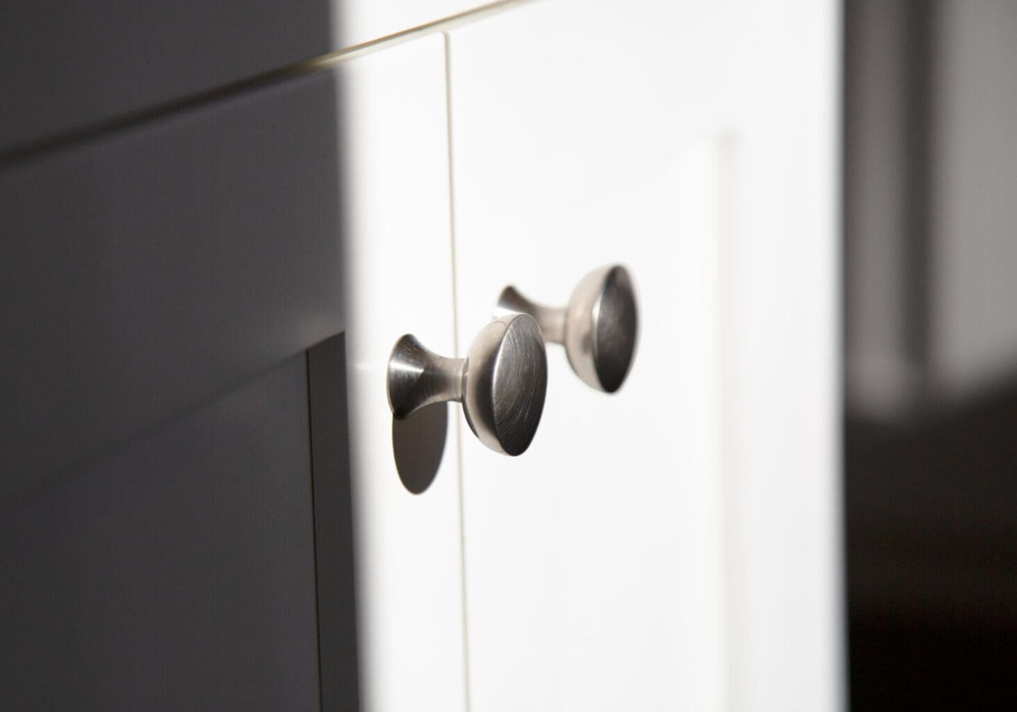 A photo of stainless steel handles on white colonial-style cabinets.