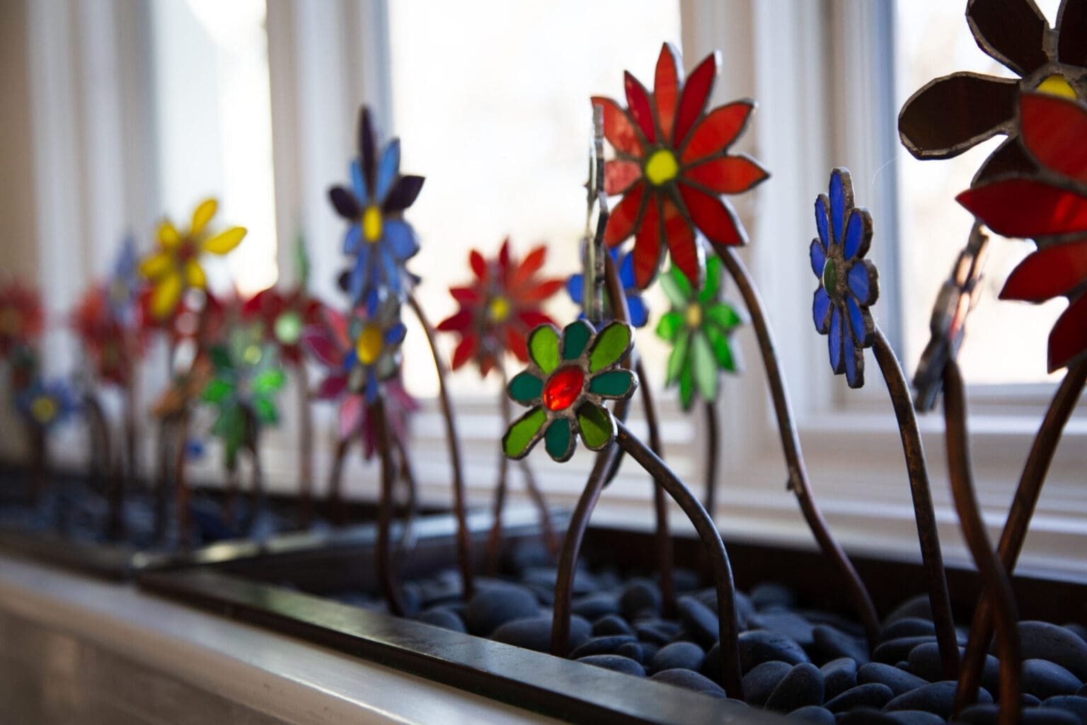 A photo of decorative multicolored stained glass flowers in front of kitchen windows.