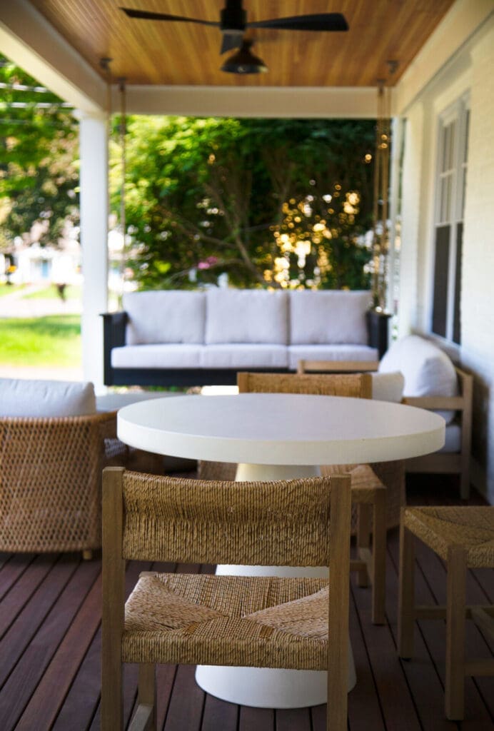 A photo of outdoor wicker and cushioned furniture on a farmer's porch with dark wood flooring and light wooden ceiling.