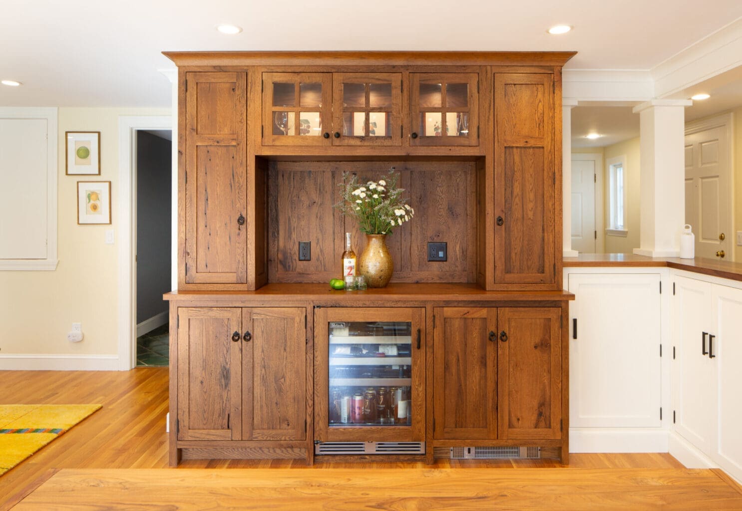 A photo of a reclaimed wooden cabinet bar with overhead cabinets and a built-in mini fridge.