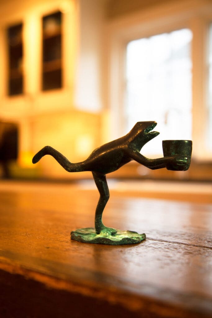 A photo of a copper frog sculpture holding a small bucket on a wooden counter.