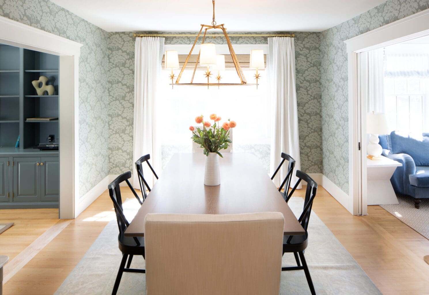 A photo of a dining room with tree-pattern wall paper and pyramid-shaped hanging light fixture.