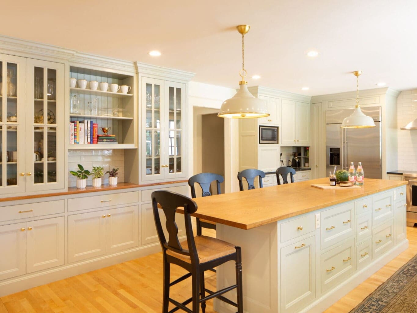 Photo of a classic grey-teal kitchen with shaker-style cabinets, brass hardware, wooden and stone countertops, and an island.