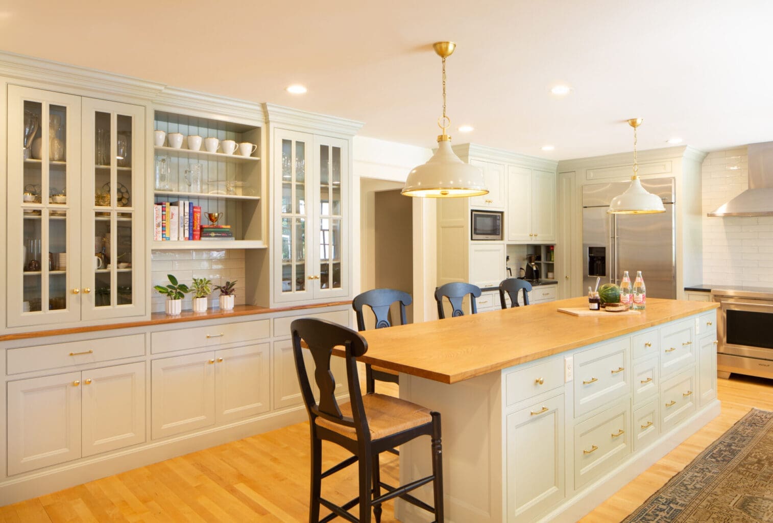 Photo of a classic grey-teal kitchen with shaker-style cabinets, brass hardware, wooden and stone countertops, and an island.