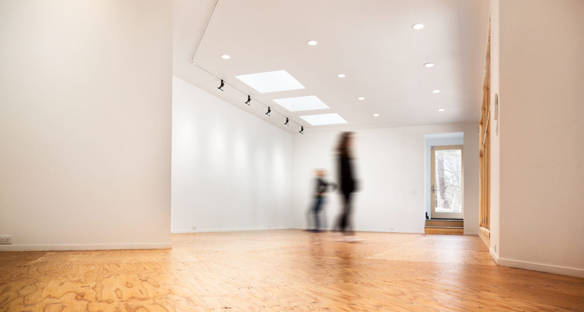 A photo of an open gallery space with white walls, skylights, recessed lighting, and spotlights.
