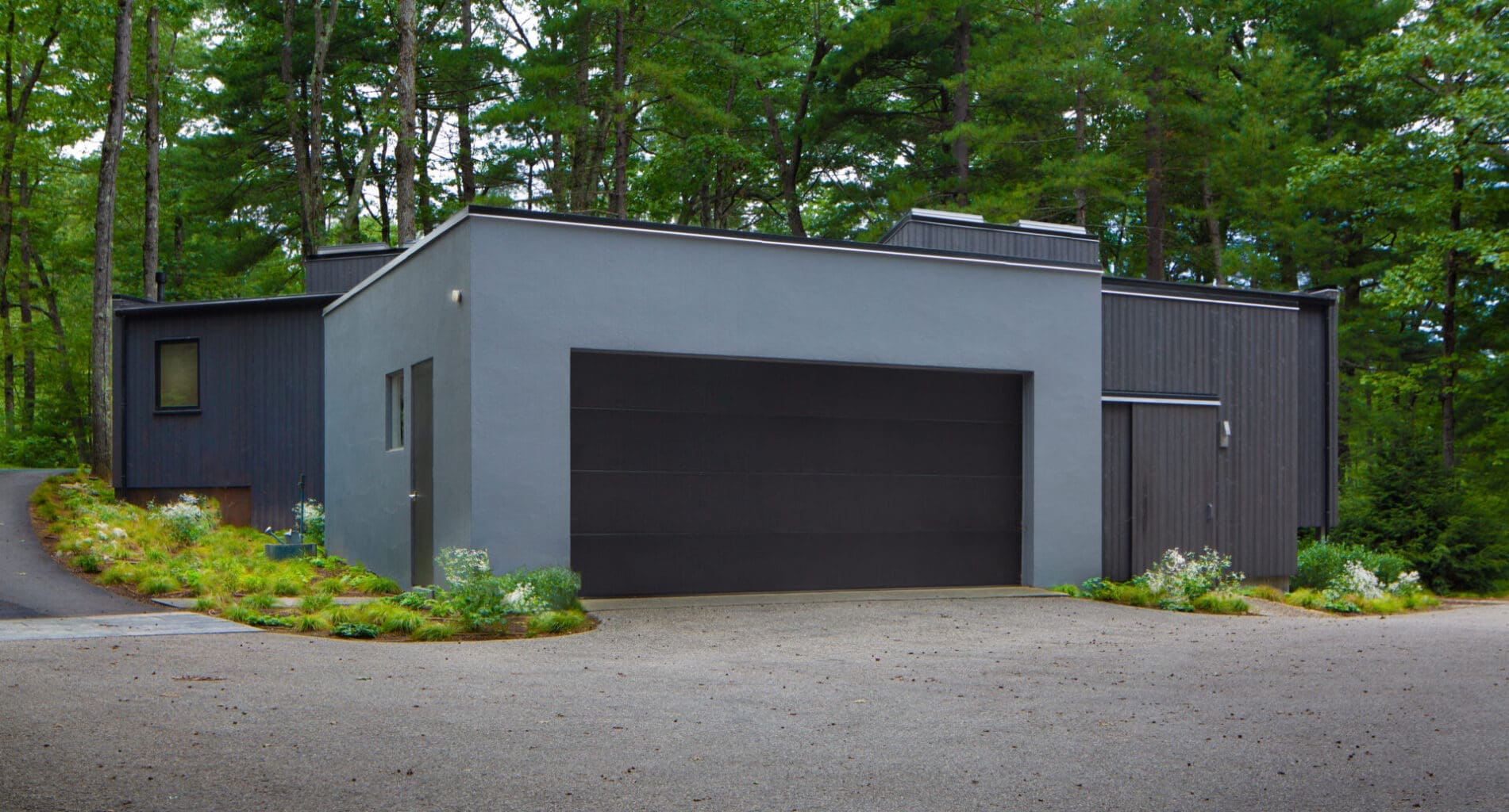 A photo of a garage with slate blue stucco finish. The rest of the building is made from 'shou sugi ban' wooden siding.