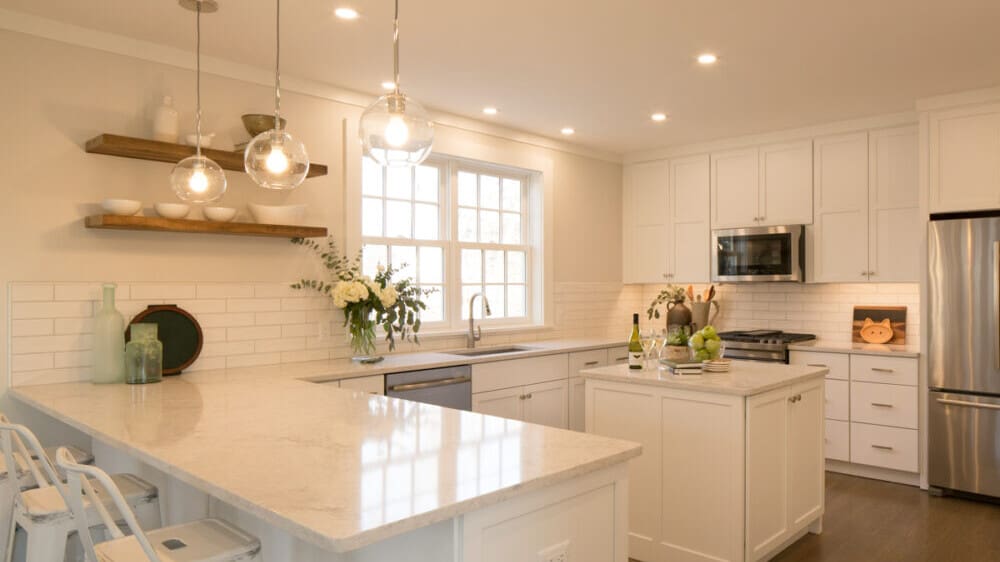 A photo of a newly renovated kitchen with white cabinetry, marble countertops, and stainless steel appliances.