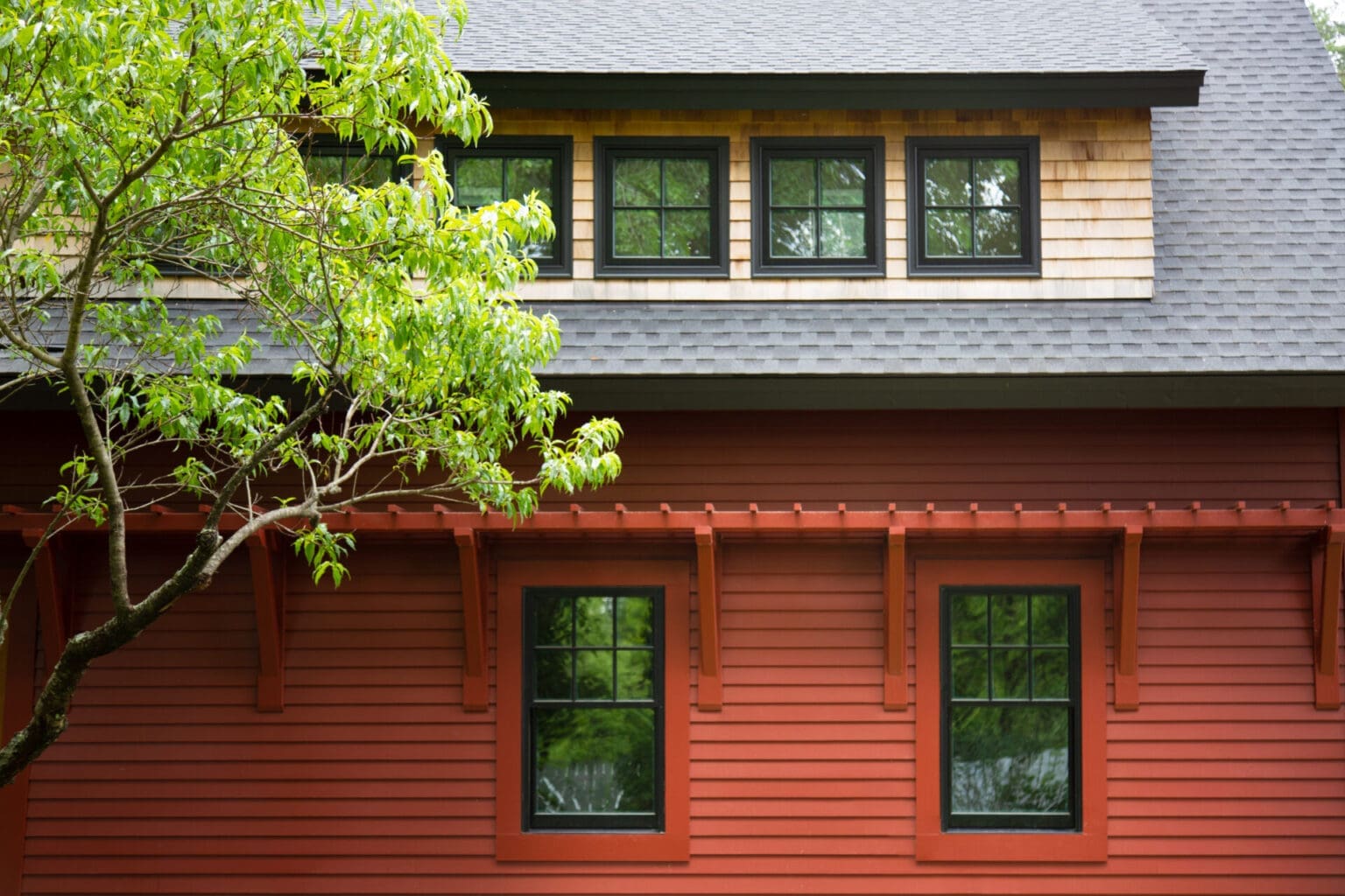 A photo of a barn-style garage with red siding, two black windows, and a red cedar second level, with square windows.