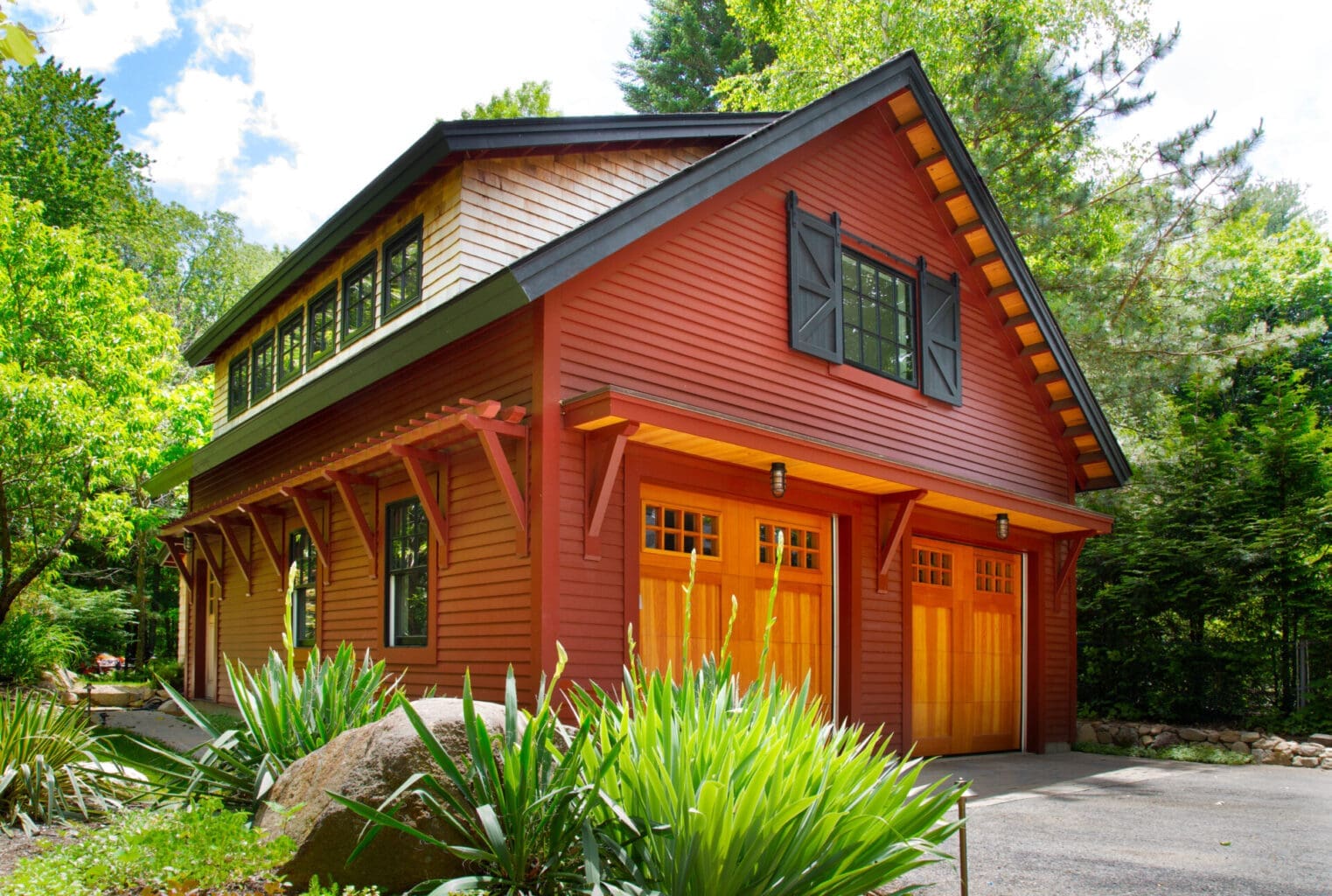 A photo of a barn-style garage with red siding, a red cedar second level, and clear vertical grain fir wooden garage doors.