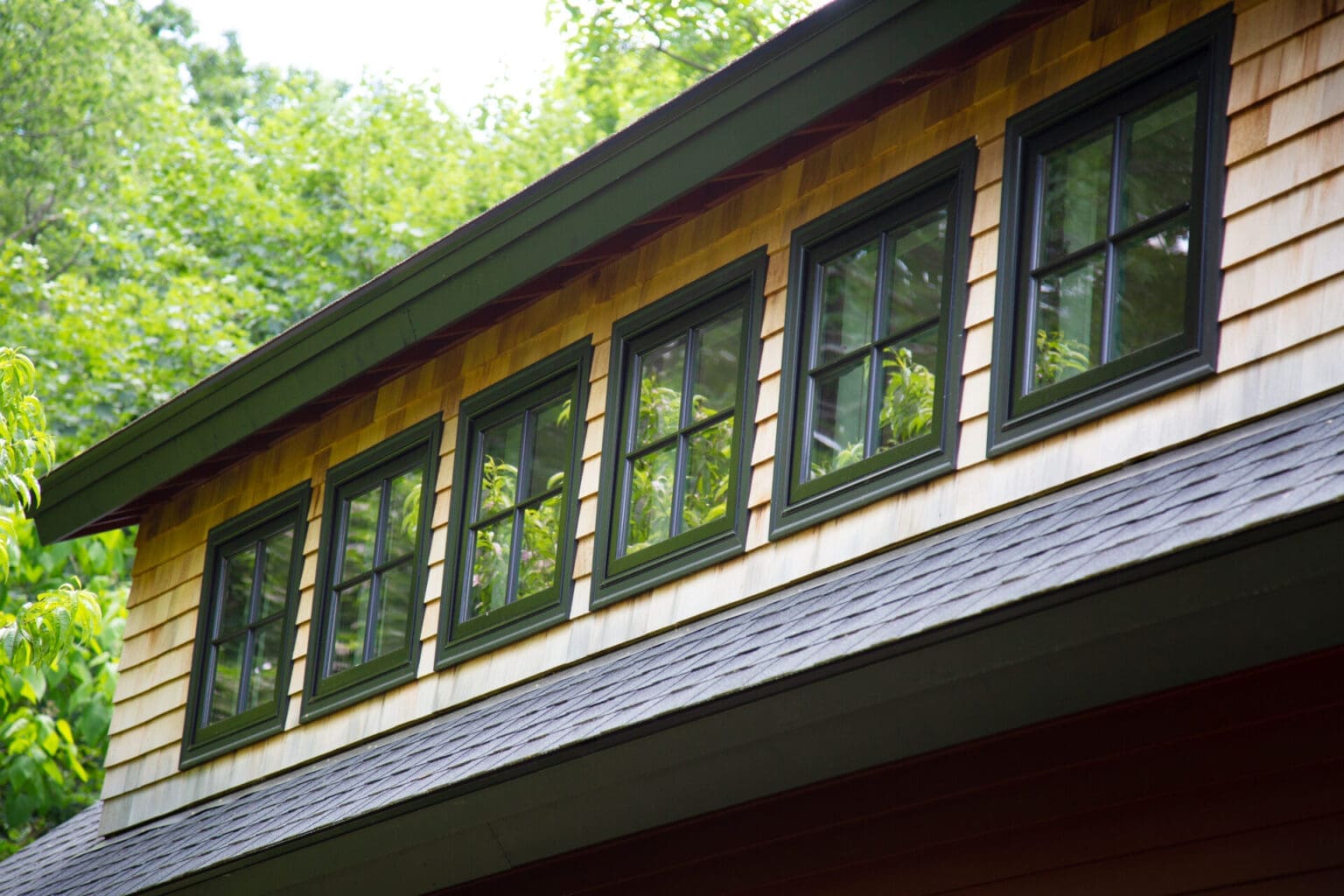 A photo of forest green windows on the second level of a garage with red cedar siding.